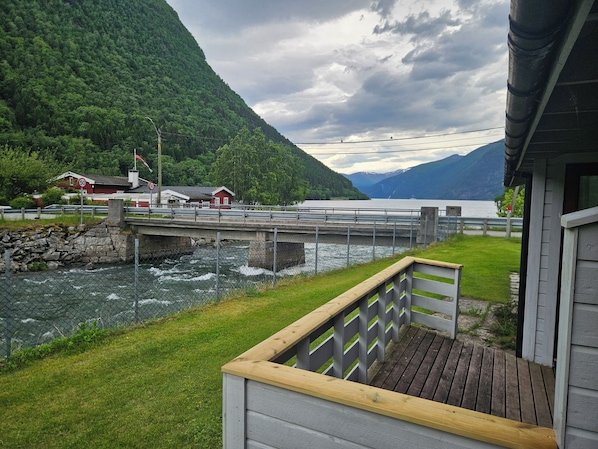 A wooden deck with a railing, a river, a bridge, and a mountain backdrop.