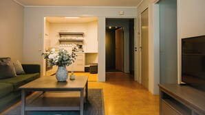 A living room with a sofa, a coffee table with a vase, a kitchen area with cabinets and a countertop, and a hallway leading to a door. - Norddalstunet (Norddal)