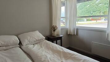 A bedroom with a bed, a nightstand, a vase with flowers, and a window with curtains.