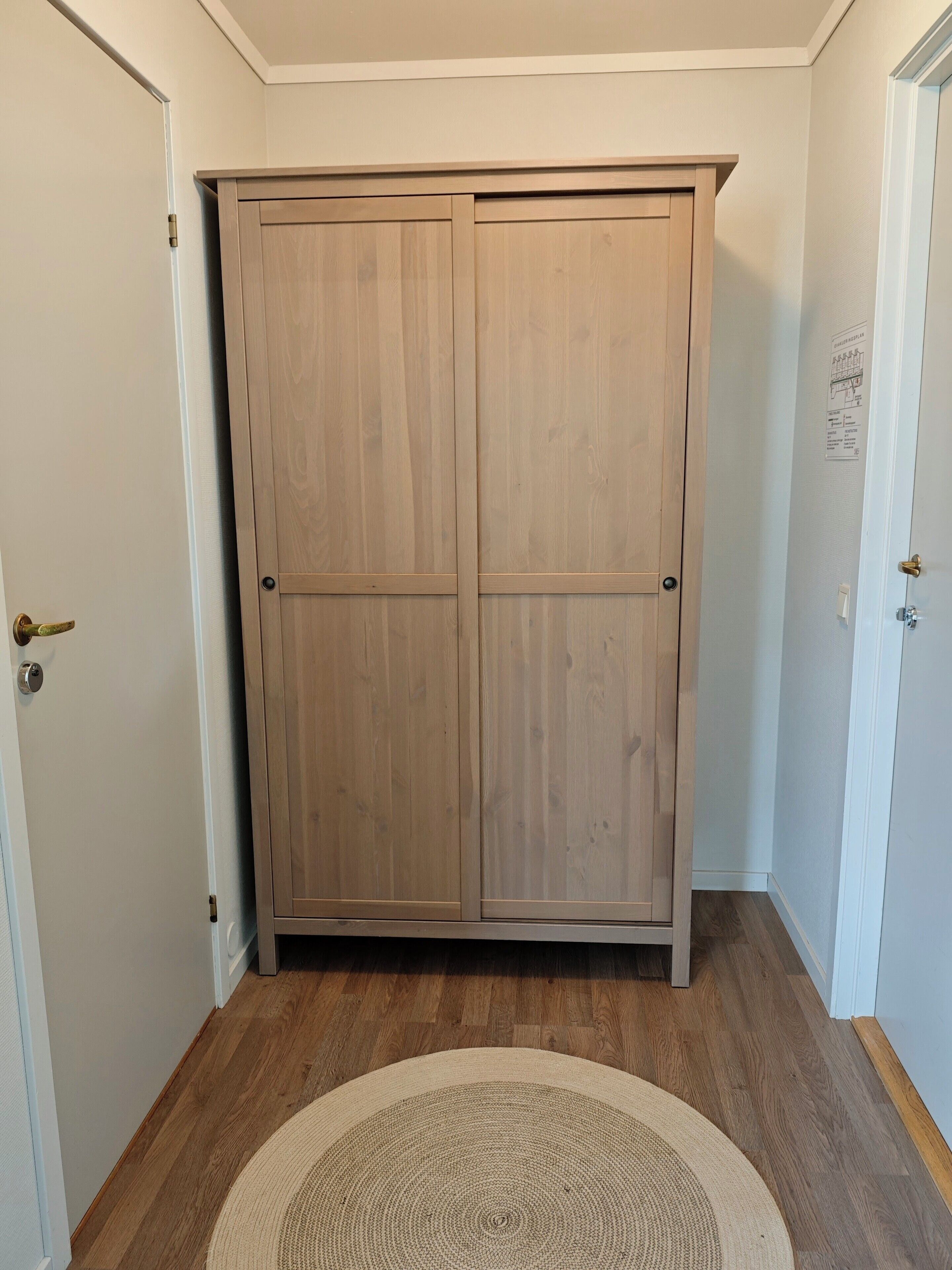 A hallway with a wooden wardrobe, a round rug, and a white door with a brass handle.