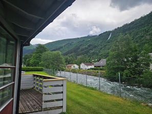 A view from a balcony overlooking a river, with houses and mountains in the background.