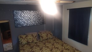 A bedroom with a patterned bedspread, a wall-mounted artwork, and a large window. - Mid-Century Charm Meets Modern Sparkle (Cedar Rapids)