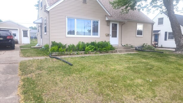 A residential house with a garage, a front yard with grass and plants, and a driveway. - Mid-Century Charm Meets Modern Sparkle (Cedar Rapids)