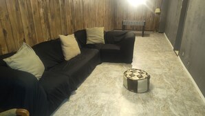 A room with a black sectional sofa, a small ottoman, a foosball table, and wooden paneling on the walls. - Mid-Century Charm Meets Modern Sparkle (Cedar Rapids)