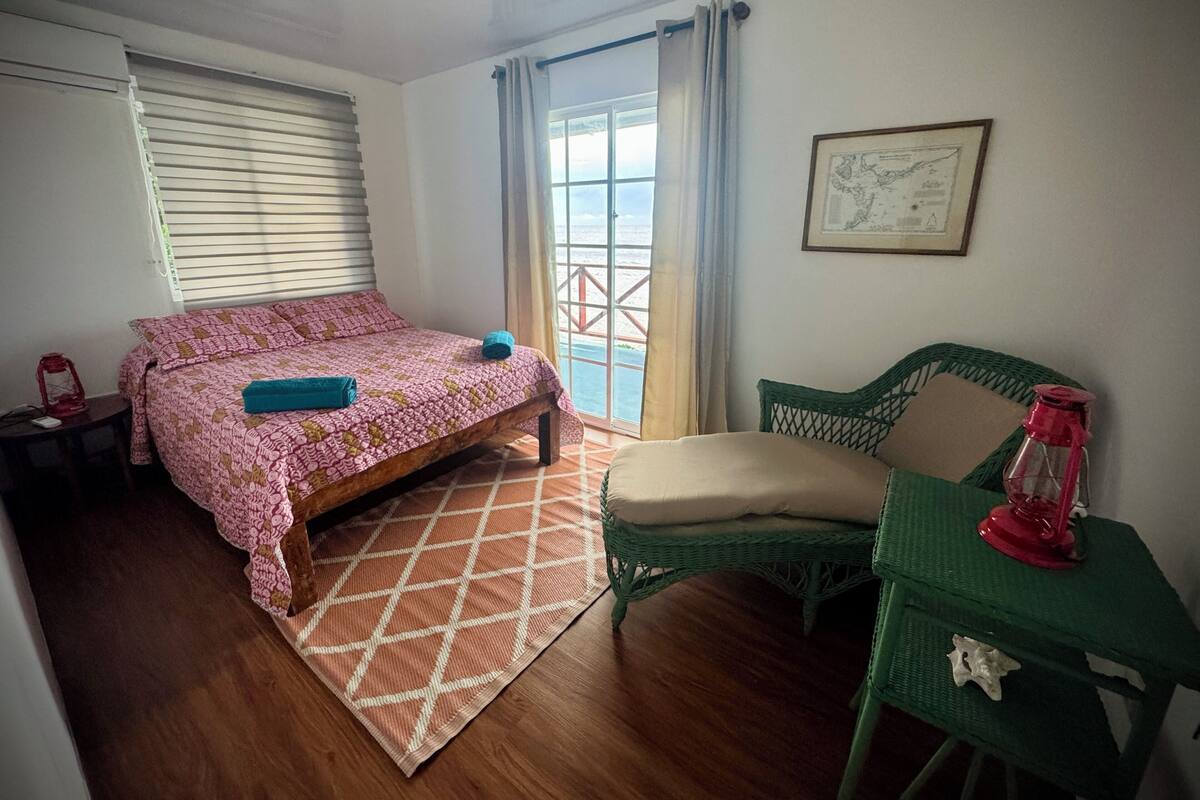 Une chambre à coucher comprenant un lit, une chaise, une table, une fenêtre avec des rideaux et une carte encadrée accrochée au mur.