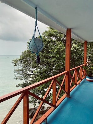 A wooden deck with a blue floor, a hanging blue hammock, and a view of the sea and trees.