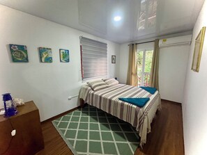Un dormitorio con una cama, una ventana con persianas, un tapete estampado verde y un aire acondicionado de pared.