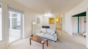 A modern living room with a sofa, a coffee table, a floor lamp, and a view through a large window. - Waterfront 2BR Condo-Walk to Iconic Seattle Spots (Seattle)