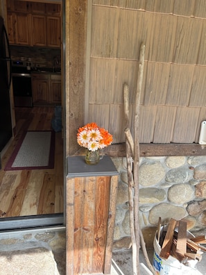 Eine rustikale Holztür mit Blumenvase, eine Steinmauer und eine Holzbank mit Holzscheiten.