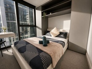 Ein modernes Schlafzimmer mit einem großen Bett, einem Schreibtisch und einem Fenster mit Blick auf die Stadt.