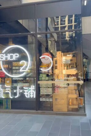 Eine Schaufensterfront mit einem großen, runden Neonzeichen mit der Aufschrift 'SHOP 2' und dem Widerschein einer Person im Fenster.