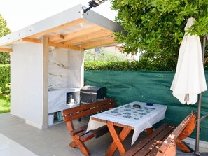 An outdoor kitchen area with a grill, a table with a patterned tablecloth, wooden benches, and a white umbrella. - Ohrid 1 by Interhome (Umag/Juricani)