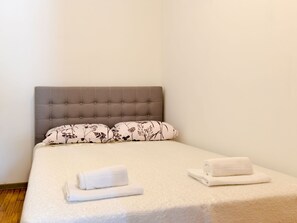 A neatly made bed with a grey upholstered headboard, two patterned pillows, and two folded white towels on the bed. - Ohrid 1 by Interhome (Umag/Juricani)