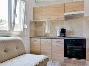 A compact kitchen with wooden cabinets, a built-in oven, and a window providing natural light. - Ohrid 1 by Interhome (Umag/Juricani)