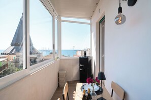 Ein Balkon mit Blick auf das Meer und Gebäude, inklusive Tisch mit Stühlen, einer Lampe und einem kleinen Schrank.