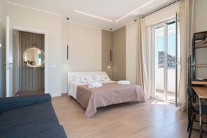 Ein modernes Hotelzimmer mit Bett, Sofa, Schreibtisch und einem Balkon mit Blick.