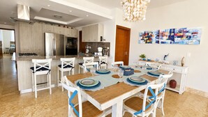 Una cucina moderna con isola centrale, sedie bianche con dettagli blu e un tavolo da pranzo per sei persone.
