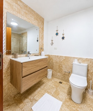 Une salle de bain avec un meuble-lavabo en bois, un lavabo blanc, des toilettes et un espace douche.