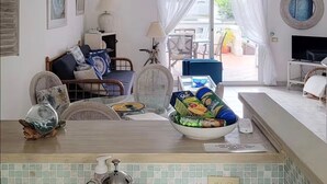Ett vardagsrum med en soffa, fåtöljer, ett matbord med en skål med snacks, en tv och en takfläkt.