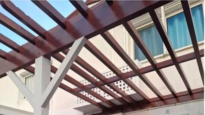 Ett takförsett utomhusområde med en pergola, en vit dörr och ett litet fönster.