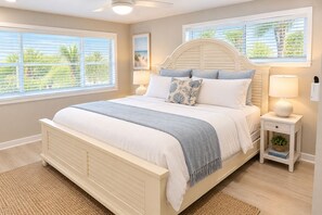 A bedroom with a bed, bedside tables, a nightstand, a lamp, and a window with blinds. - St Pete Beach house | Private Pool + Walk to Beach (St Pete Beach)