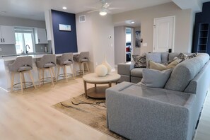 A modern living room with a grey sofa, a round coffee table, and bar stools. - Boca Ciega Isle 3BR | Pool + Walk to Beach | Private House (St Pete Beach)