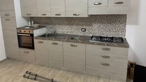 Une cuisine équipée d’un four encastré, d’une cuisinière à gaz, d’un évier et de meubles de rangement en bois clair.