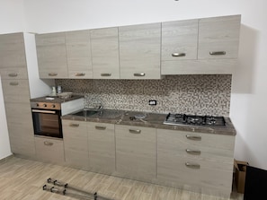 Una cucina con forno a incasso, piano cottura a gas, lavello e mobili in legno chiaro.