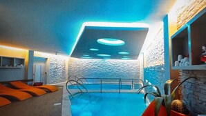 En indendørs swimmingpool med moderne design, der inkluderer en stenvæg og et loft med runde lys.