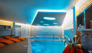 Una piscina interna dal design moderno, con una parete in pietra e un soffitto illuminato da luci circolari.
