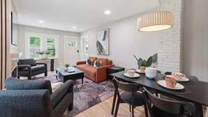 Een moderne woonkamer met een bank, stoelen, een eettafel met kopjes en een hanglamp.