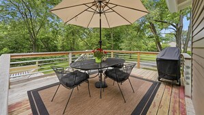 Een terras met een tafel, stoelen, een parasol en een barbecue.