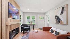 Un salon moderne avec un téléviseur à écran plat, un canapé, un fauteuil et un tableau accroché au mur.