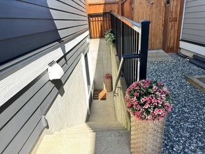 Escadaria de concreto que leva a um deck de madeira, com corrimão de metal e um vaso de flores cor-de-rosa.