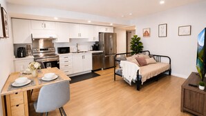 A modern kitchen with white cabinets, stainless steel appliances, and a dining area with a wooden table and grey chair. - Cozy South Surrey Private One-Bedroom - 2 beds - (Surrey)