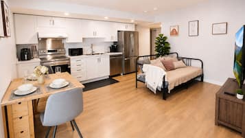 Una cucina moderna con mobili bianchi, elettrodomestici in acciaio inossidabile e un'area pranzo con tavolo in legno e sedia grigia.