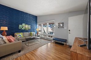 Een moderne woonkamer met een blauwe muur, een bank, een salontafel, een zitbank en een televisie op een houten meubel.