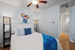 Une chambre à coucher comprenant un lit, un ventilateur de plafond, une œuvre d’art accrochée au mur et une table de chevet avec une lampe.