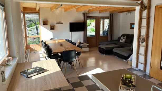 Un intérieur moderne avec une table à manger en bois, des chaises noires, un canapé et un téléviseur.