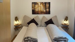 Une chambre à coucher avec un lit en bois, une literie à carreaux, une décoration murale sur le thème de la forêt et des lampes de chevet.