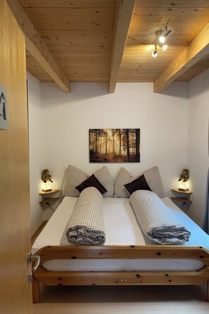 A bedroom with a wooden bed, checkered bedding, a forest-themed wall art, and bedside lamps. - Ferienhaus La Trapla, (Samnaun-Compatsch) by Interhome (Samnaun)