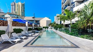 Une piscine avec des chaises longues, un espace abrité et une vue sur les immeubles de grande hauteur.