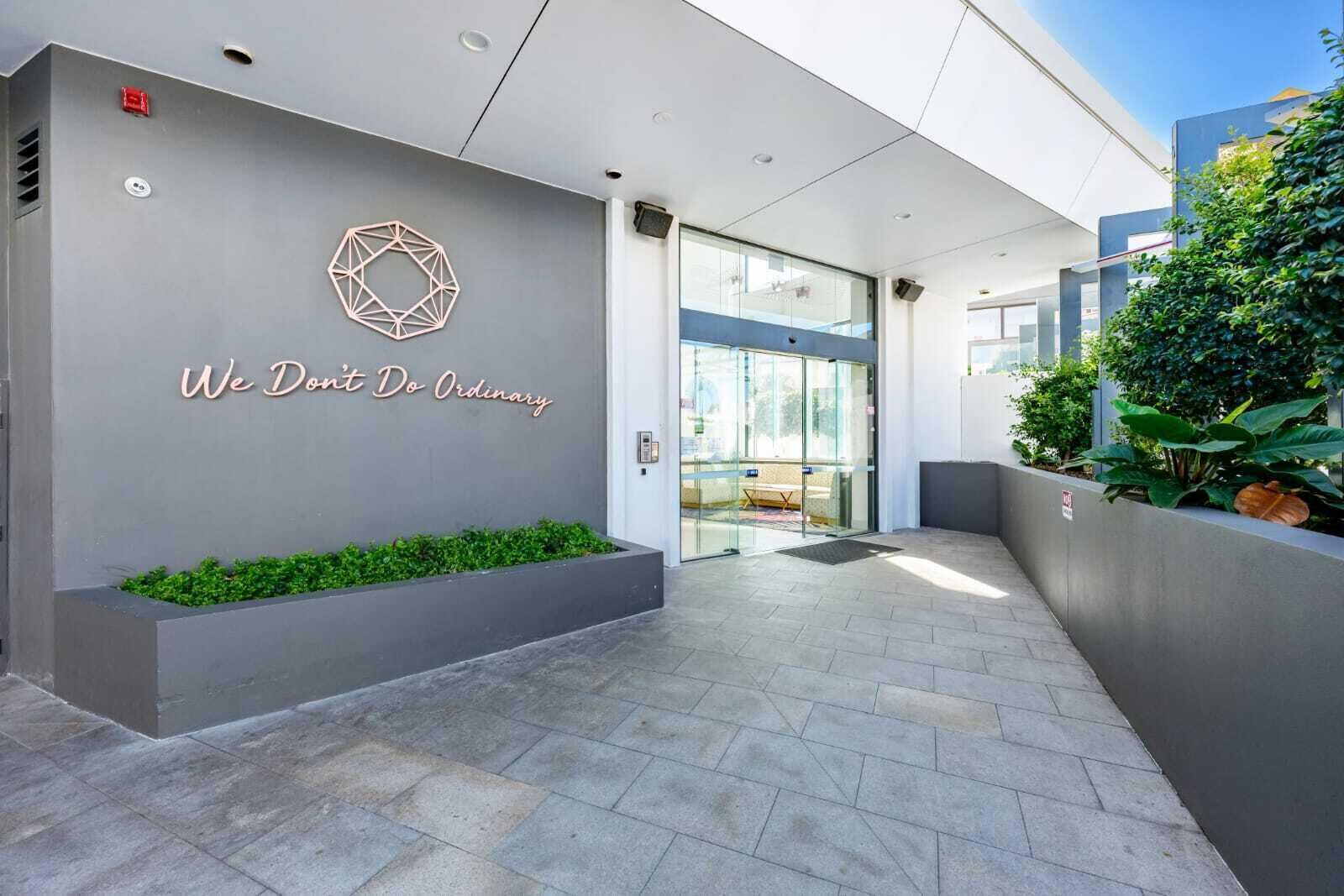 A modern building entrance with a geometric wall design, a glass door, and a pathway leading to the interior.