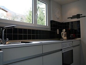A kitchen with a window, black tiled backsplash, and a clock on the wall. - Brentsch Park, (Scuol) by Interhome (Scuol)