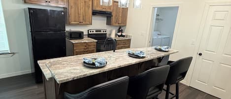 A kitchen with wooden cabinets, a black refrigerator, a marble countertop, and pendant lights.