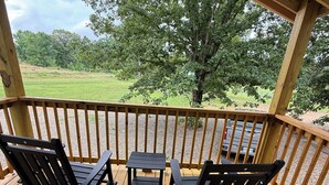 A wooden deck with two rocking chairs and a small table, overlooking a grassy area with trees.