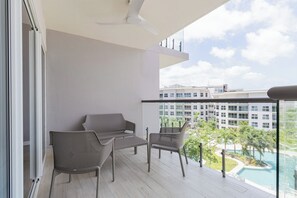 Ein Balkon mit einer Couch und Stühlen, einem Deckenventilator sowie Blick auf einen Gebäudekomplex und einen Swimmingpool.