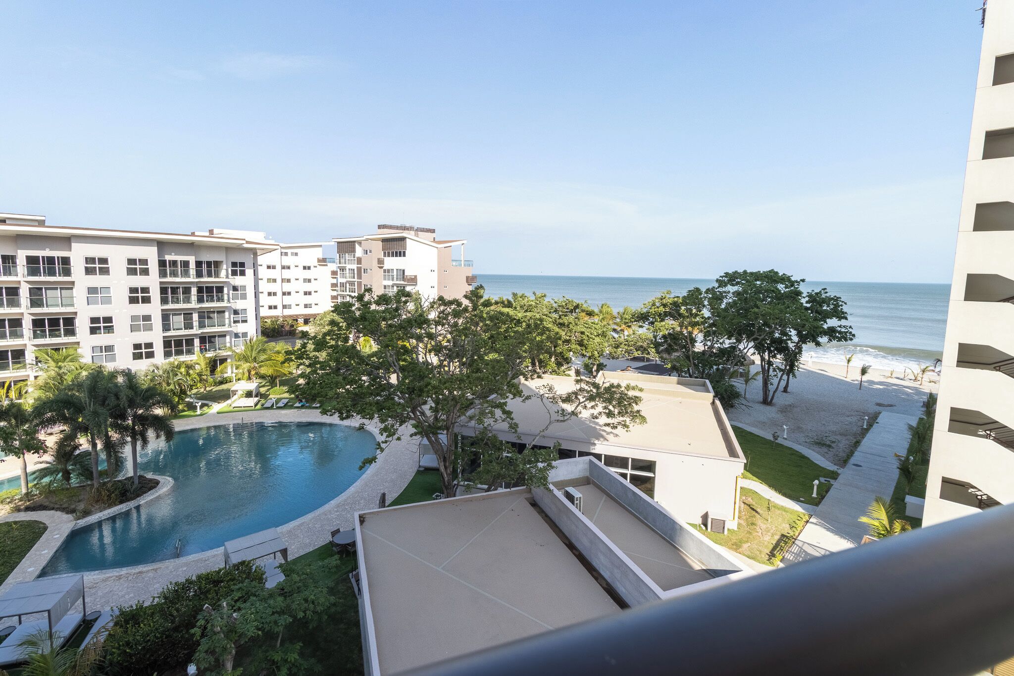 Un hôtel doté d’une piscine, offrant une vue sur la plage et comprenant un espace paysager avec des arbres.