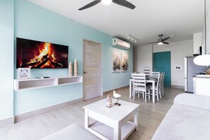 Ein modernes Wohnzimmer mit Flachbildfernseher, weißen Möbeln, Deckenventilator und Klimaanlage.