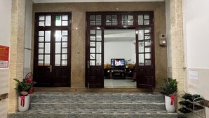 A hotel lobby with two wooden doors, a patterned carpet, and potted plants.